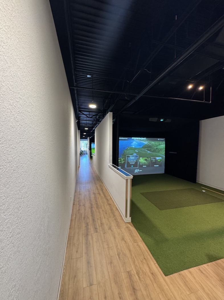 A finished simulator bay off the main corridor, with synthetic turf hitting area and new wood-look flooring.